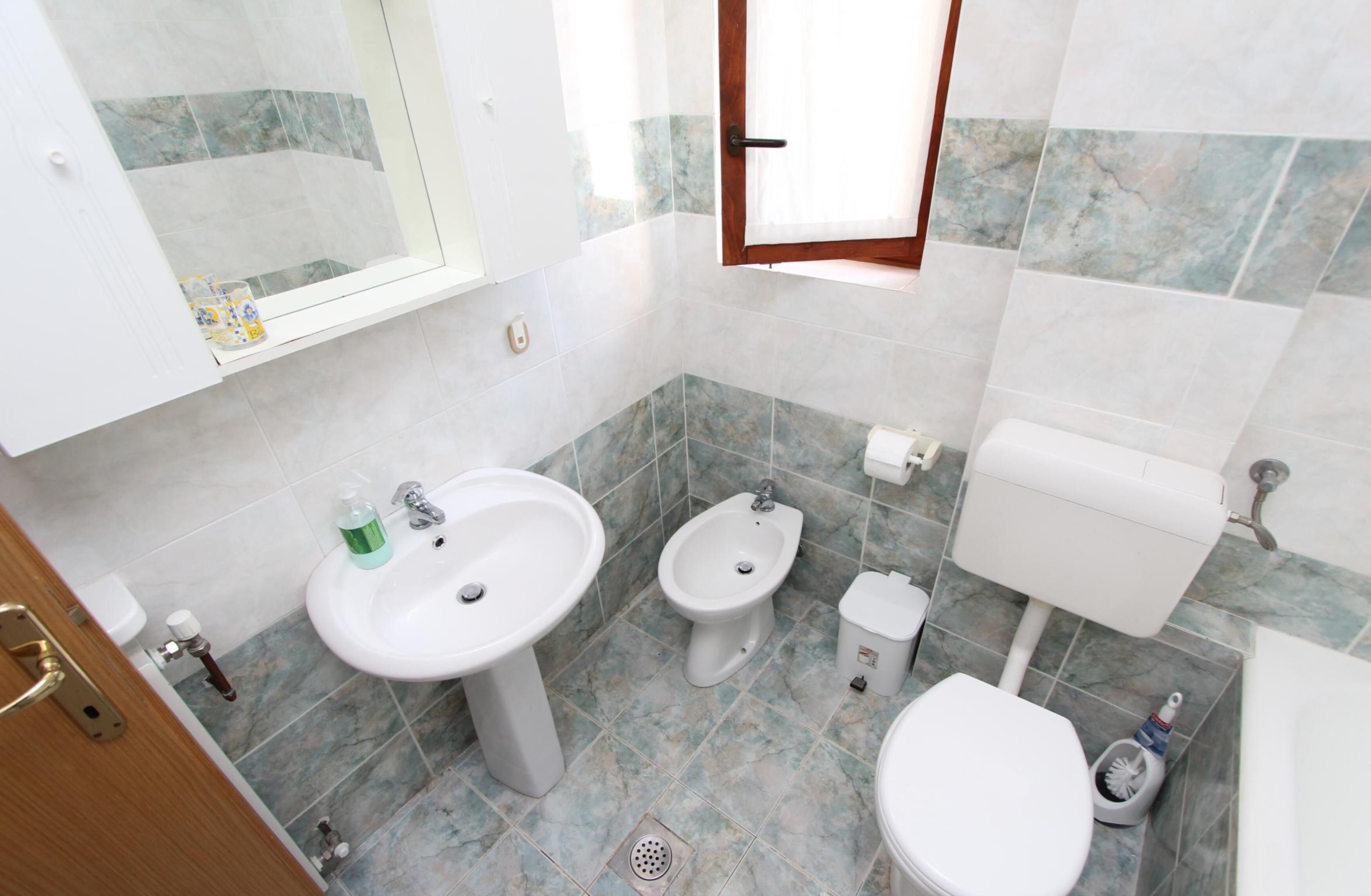 A bathroom with a sink, bidet, toilet, and a window.