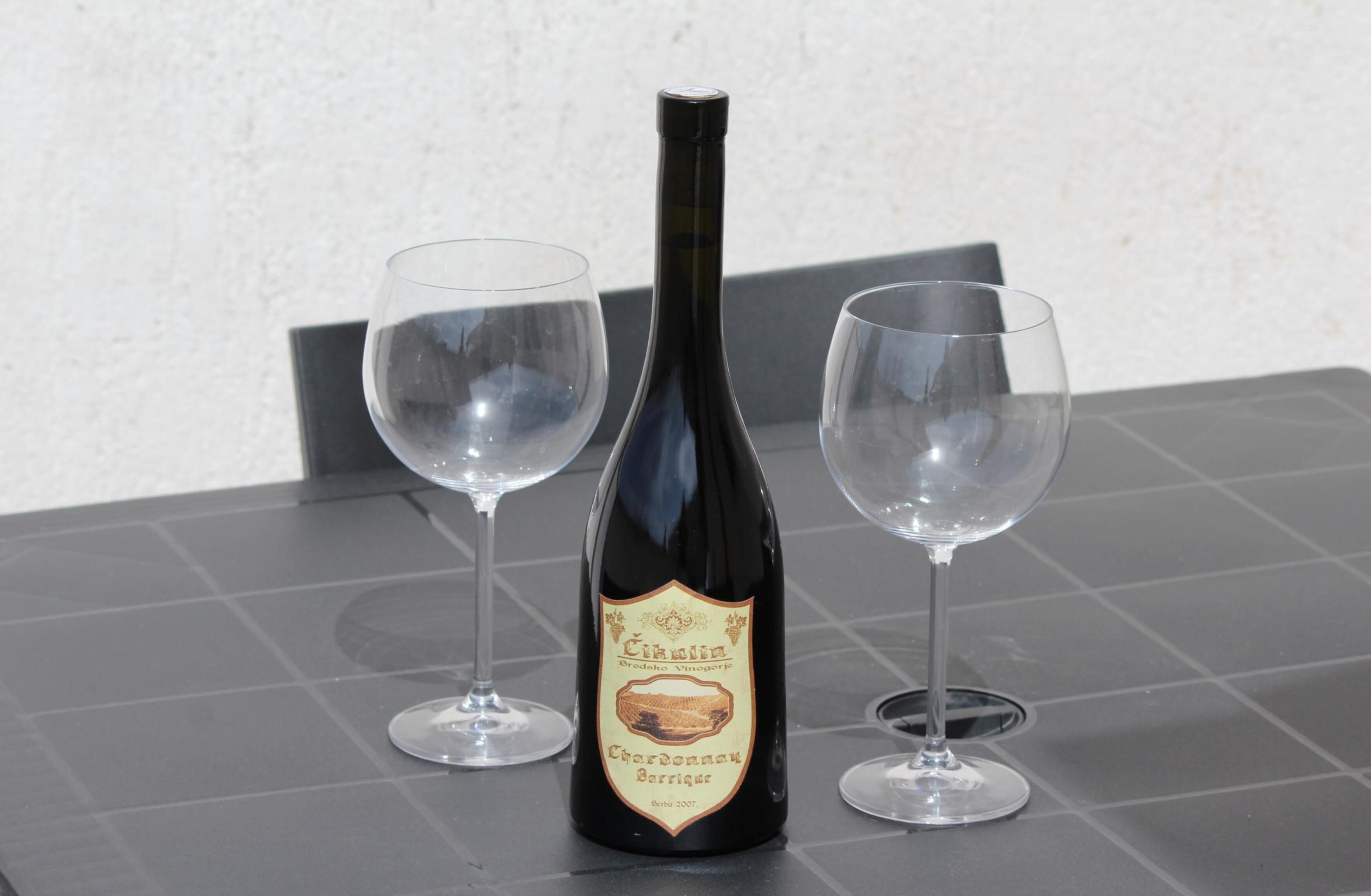 Una botella de vino con dos copas vacías sobre una superficie con baldosas.