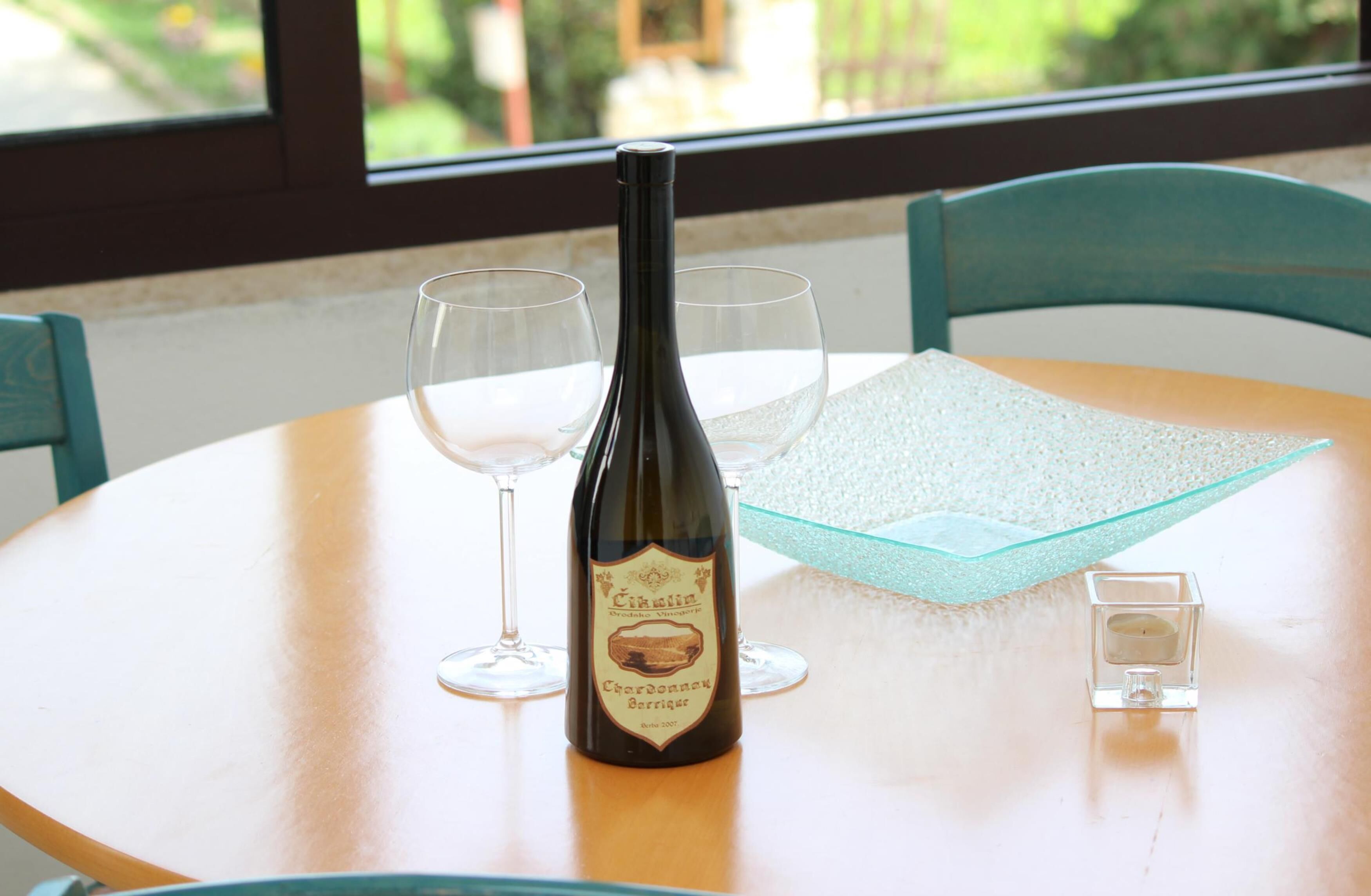 Una botella de vino sobre una mesa con dos copas y un cuenco de cristal.