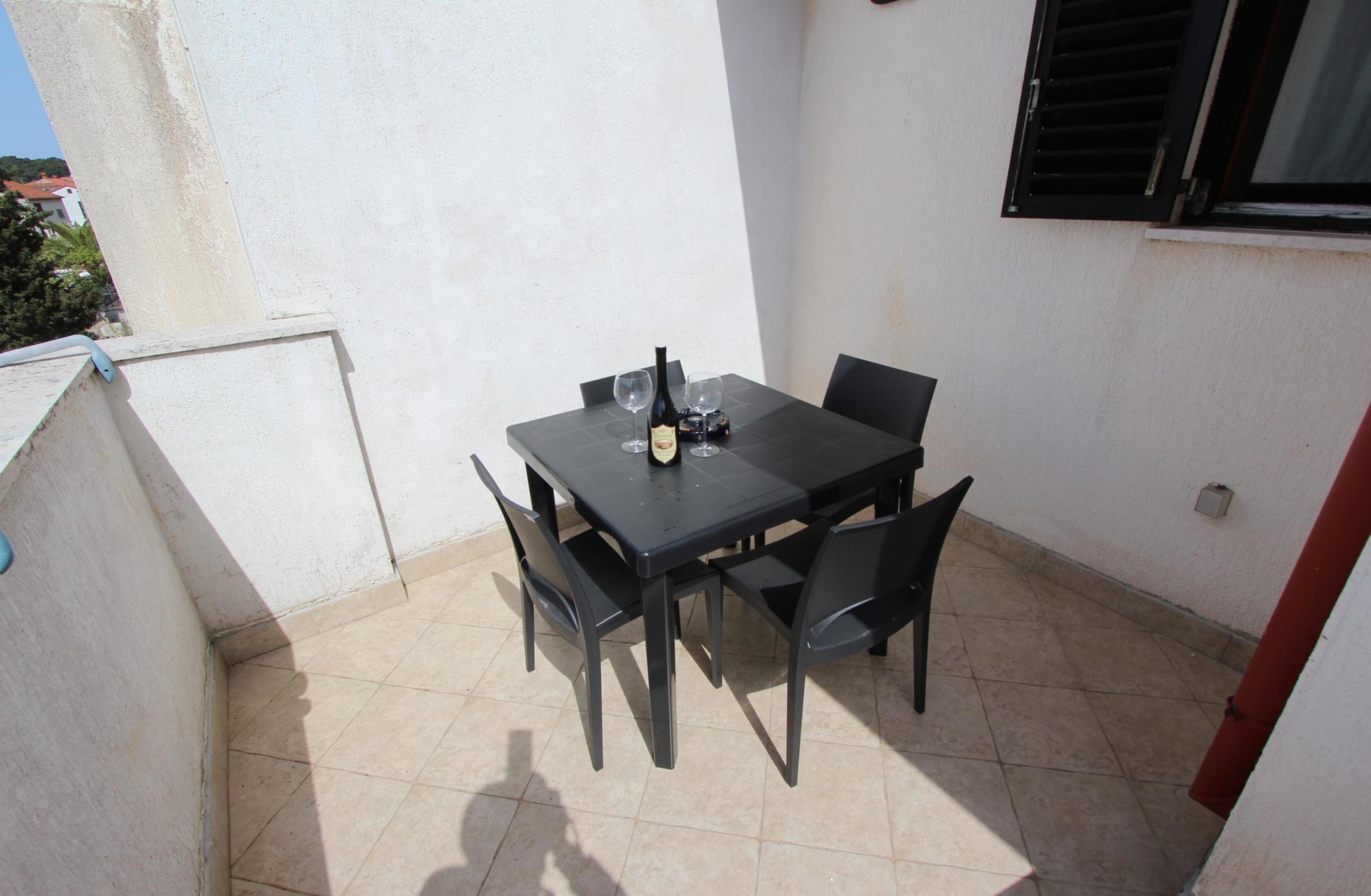 Eine kleine Terrasse im Freien mit Tisch und Stühlen, einer Weinflasche und einem Fenster mit Rollläden.