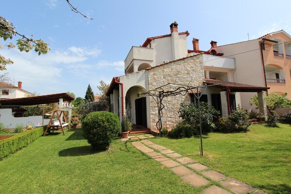 A two-story house with a stone facade, a red-tiled roof, and a small garden with a pathway leading to the entrance. - Apartments Milena (Rovinj)
