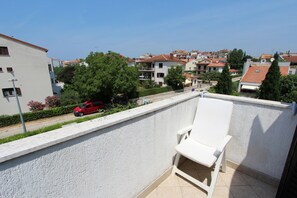 A balcony with a white chair, a red car parked on the street, and buildings in the background. - Apartments Milena (Rovinj)