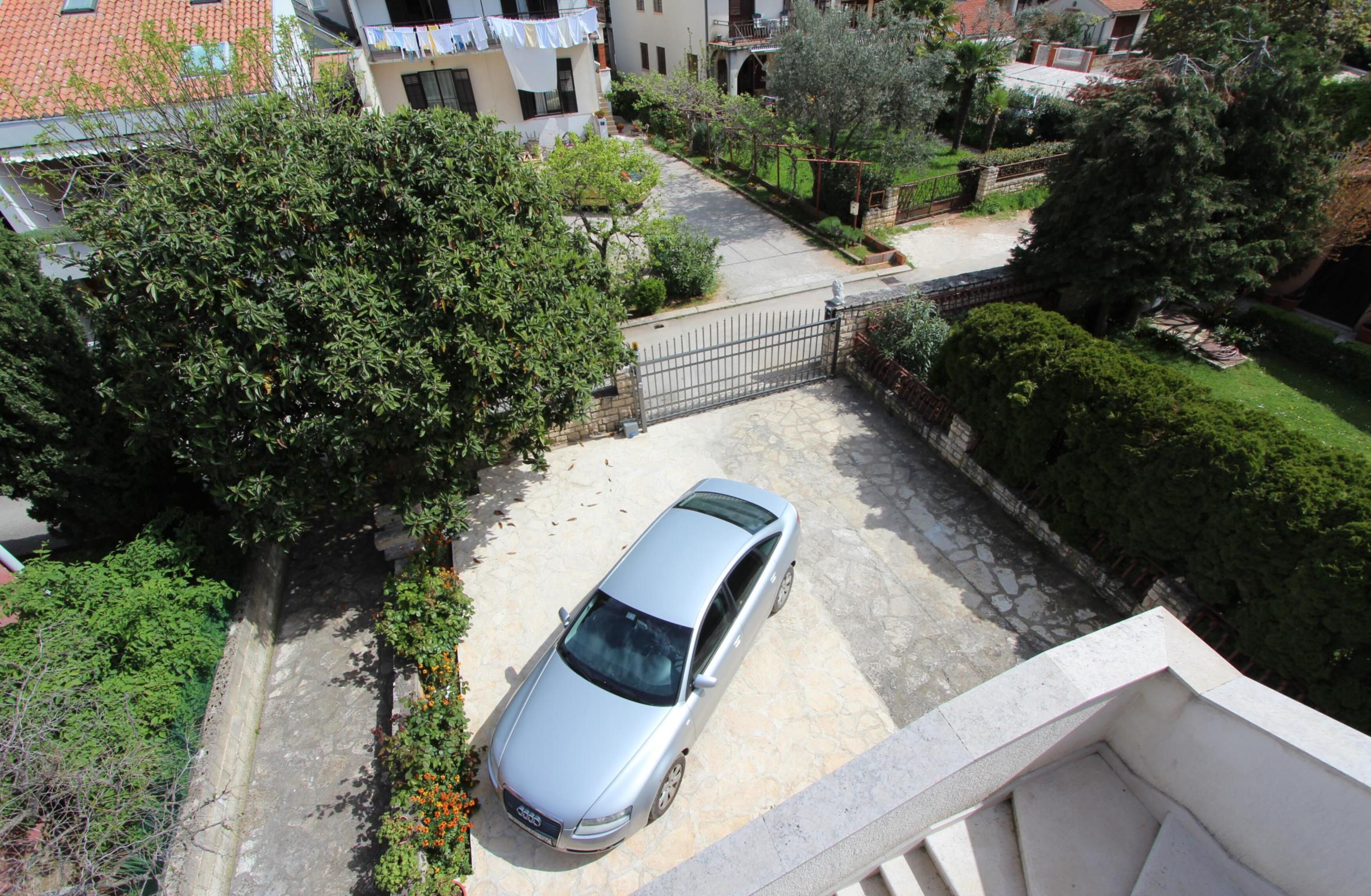 Un quartier résidentiel avec une voiture garée, une entrée fermée par un portail et un escalier menant à un balcon.