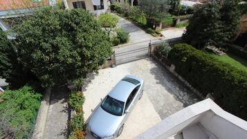 Un quartier résidentiel avec une voiture garée, une entrée fermée par un portail et un escalier menant à un balcon.