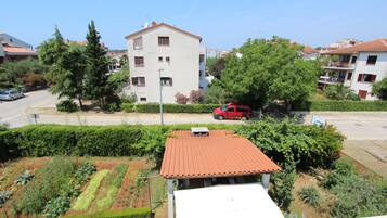 Un quartiere residenziale con un edificio bianco dotato di tetto rosso, immerso nel verde e affiancato da una strada con un'auto rossa parcheggiata.