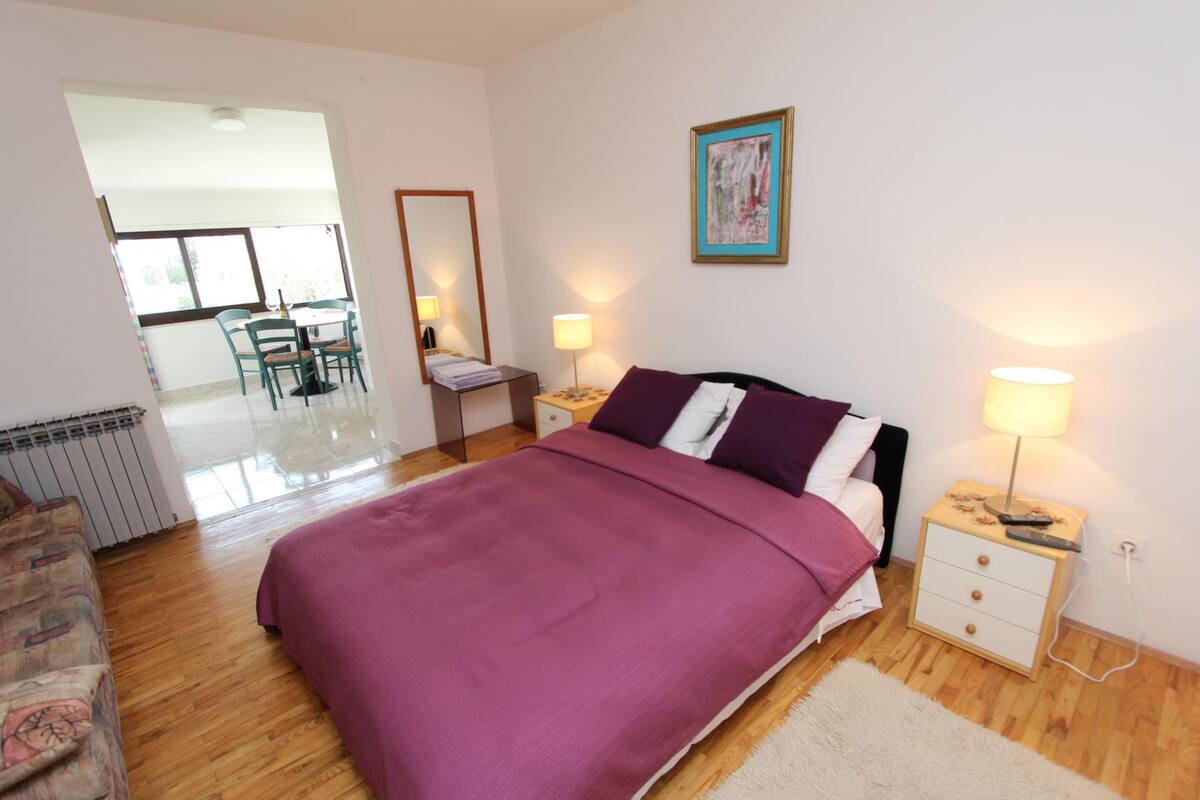 Een slaapkamer met een bed, nachtkastjes, een stoel, een lamp en een schilderij aan de muur.