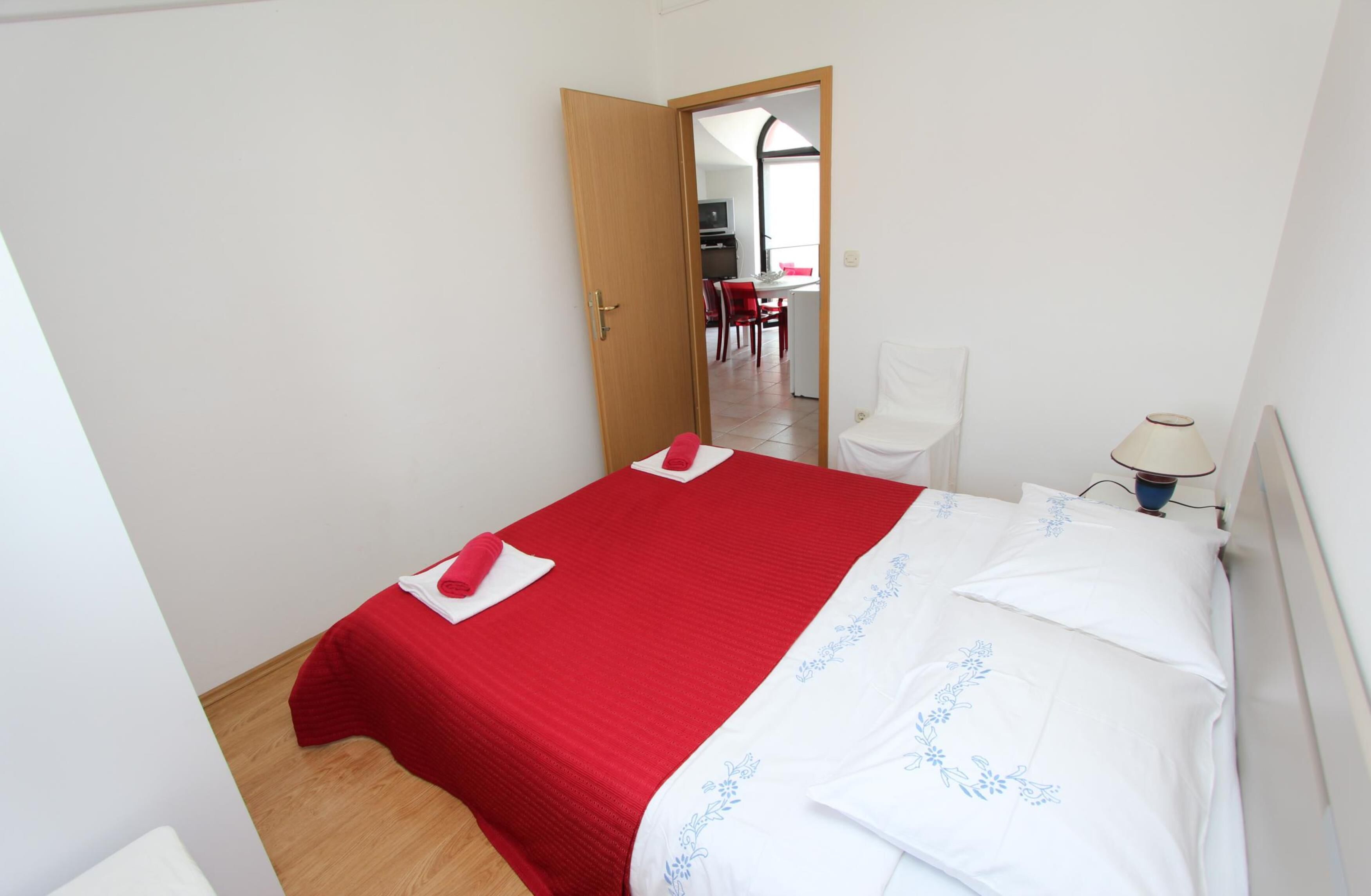 Un dormitorio con cama, una puerta de madera, una silla y un escritorio con su silla.