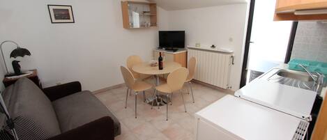 A compact living space with a sofa, dining table, chairs, a TV, and a kitchenette.
