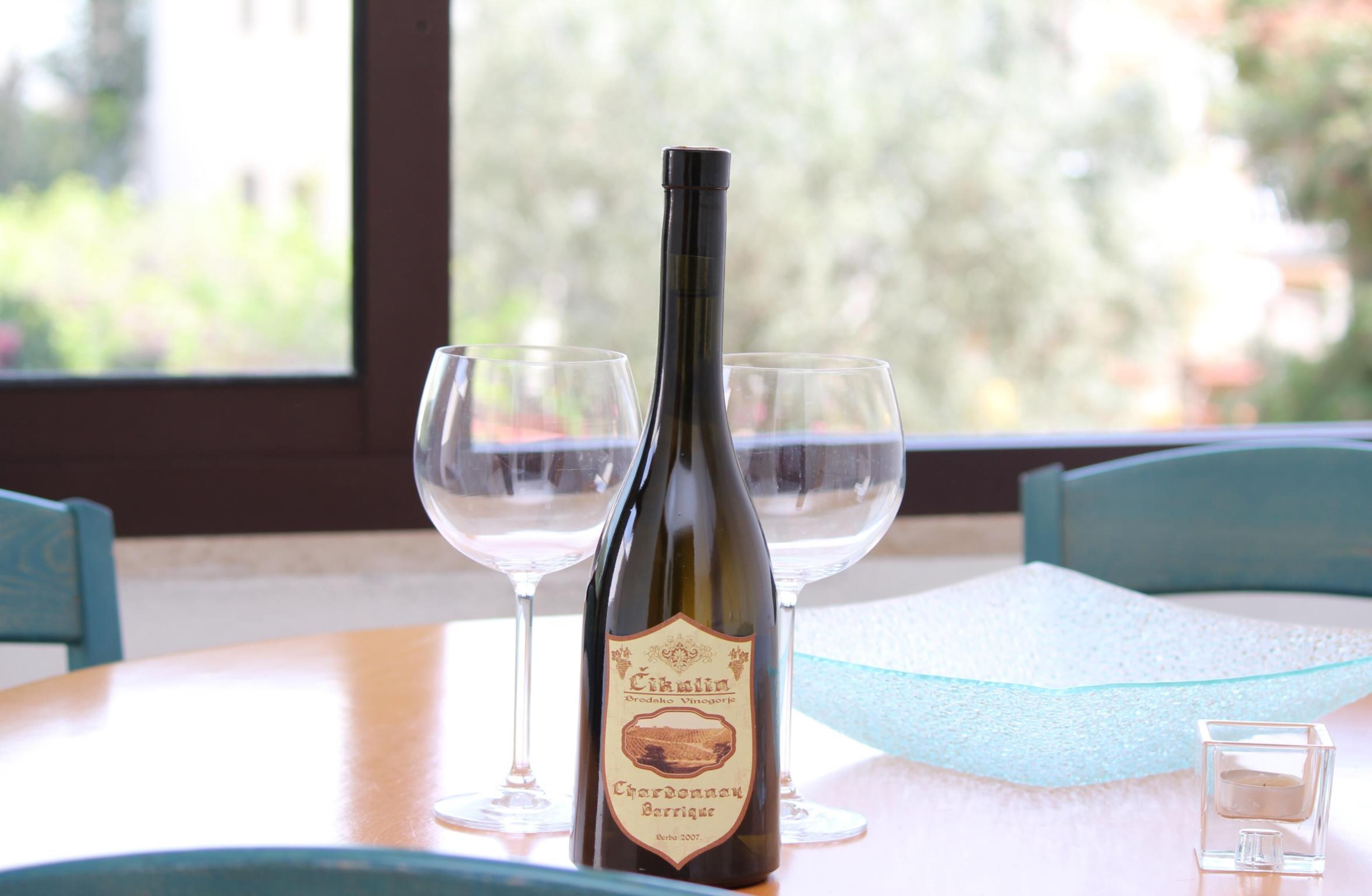 Een fles wijn en twee glazen op een tafel, met uitzicht op bomen door een raam.