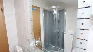 A modern bathroom with a glass-enclosed shower, a glass-topped vanity, and a white cabinet with drawers.