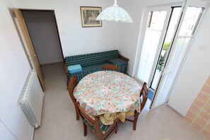 A dining area with a round table, chairs, a patterned tablecloth, a bench, and a door leading outside. - Apartments Milka (Rovinj)