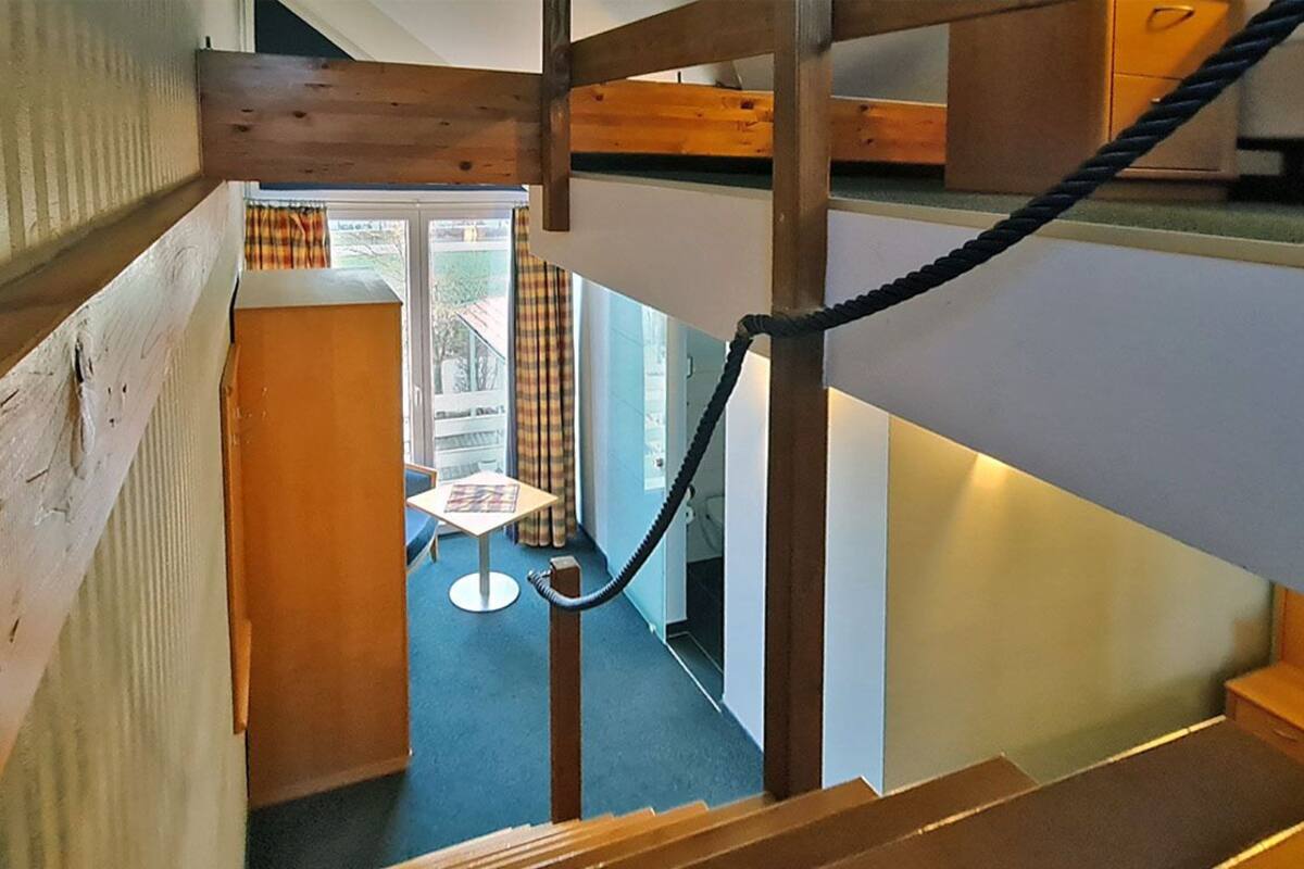 A staircase with wooden beams and a rope handrail leading to a room with a small table and chairs.