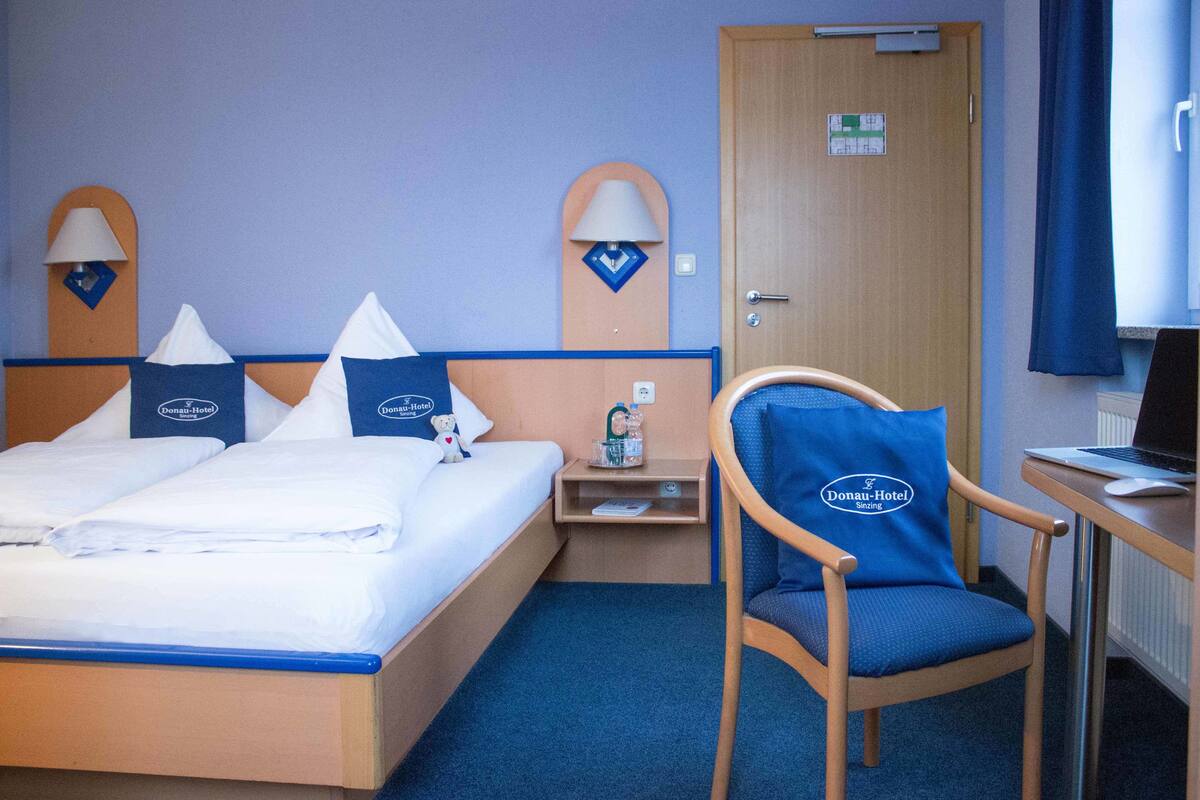 A hotel room with a bed, a chair, a desk, and a door.