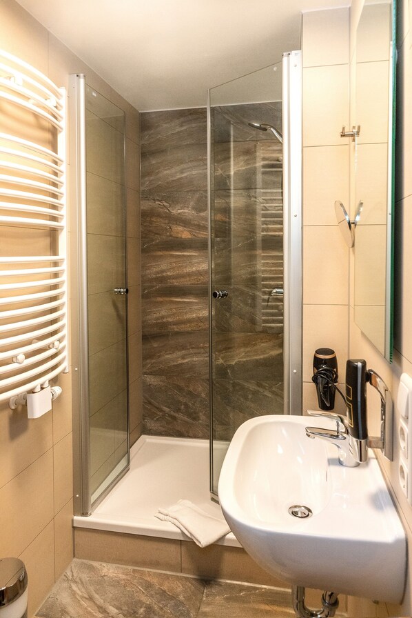 A modern bathroom with a glass-enclosed shower, a white sink, and a towel rack.