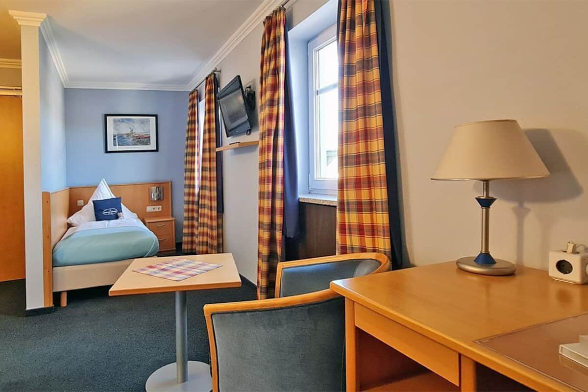 A hotel room with a bed, a desk, a chair, a table, a TV, and curtains.