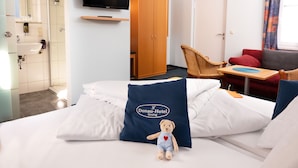 Hotellihuone, jossa on sänky, televisio, vaatekaappi, tuoli ja pieni pöytä.