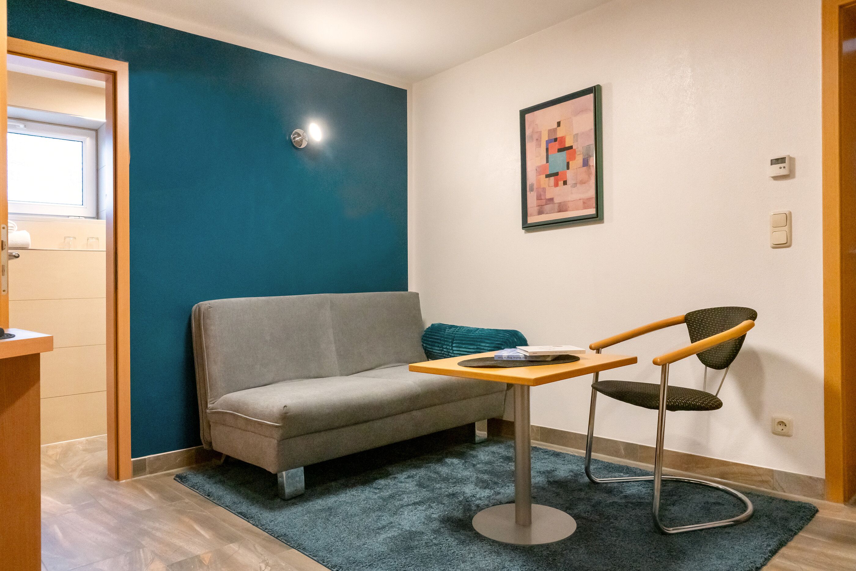 Una habitación pequeña con un sofá gris, una mesa de madera, una silla verde y un tapete azul.
