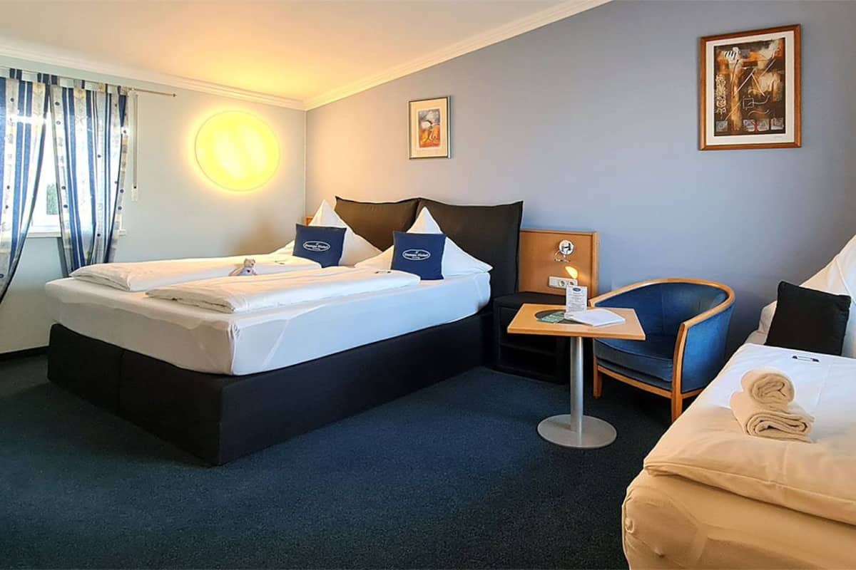 A hotel room with a double bed, a single bed, a desk, and a chair.