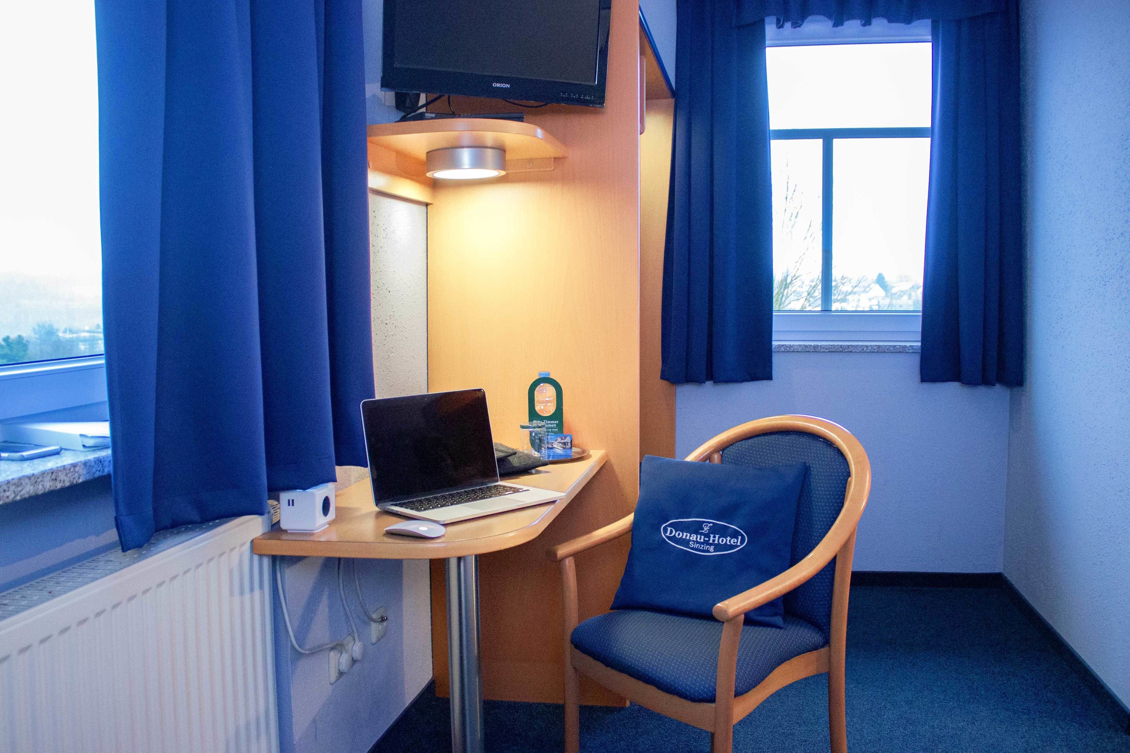 Una habitación de hotel pequeña con escritorio, ordenador portátil, silla y televisión montada en la pared.