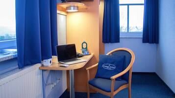 Una habitación de hotel pequeña con escritorio, ordenador portátil, silla y televisión montada en la pared.