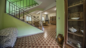 A staircase with a green railing leading to a second floor, a patterned floor, and a cabinet with dishes. - Residenzadelia (Ronciglione)