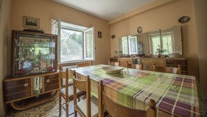 A dining area with a table set for four, surrounded by wooden chairs. A glass cabinet with dishes is to the left. - Residenzadelia (Ronciglione)