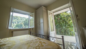A bedroom with a bed, a wardrobe, a radiator, and a balcony with a view of greenery. - Residenzadelia (Ronciglione)