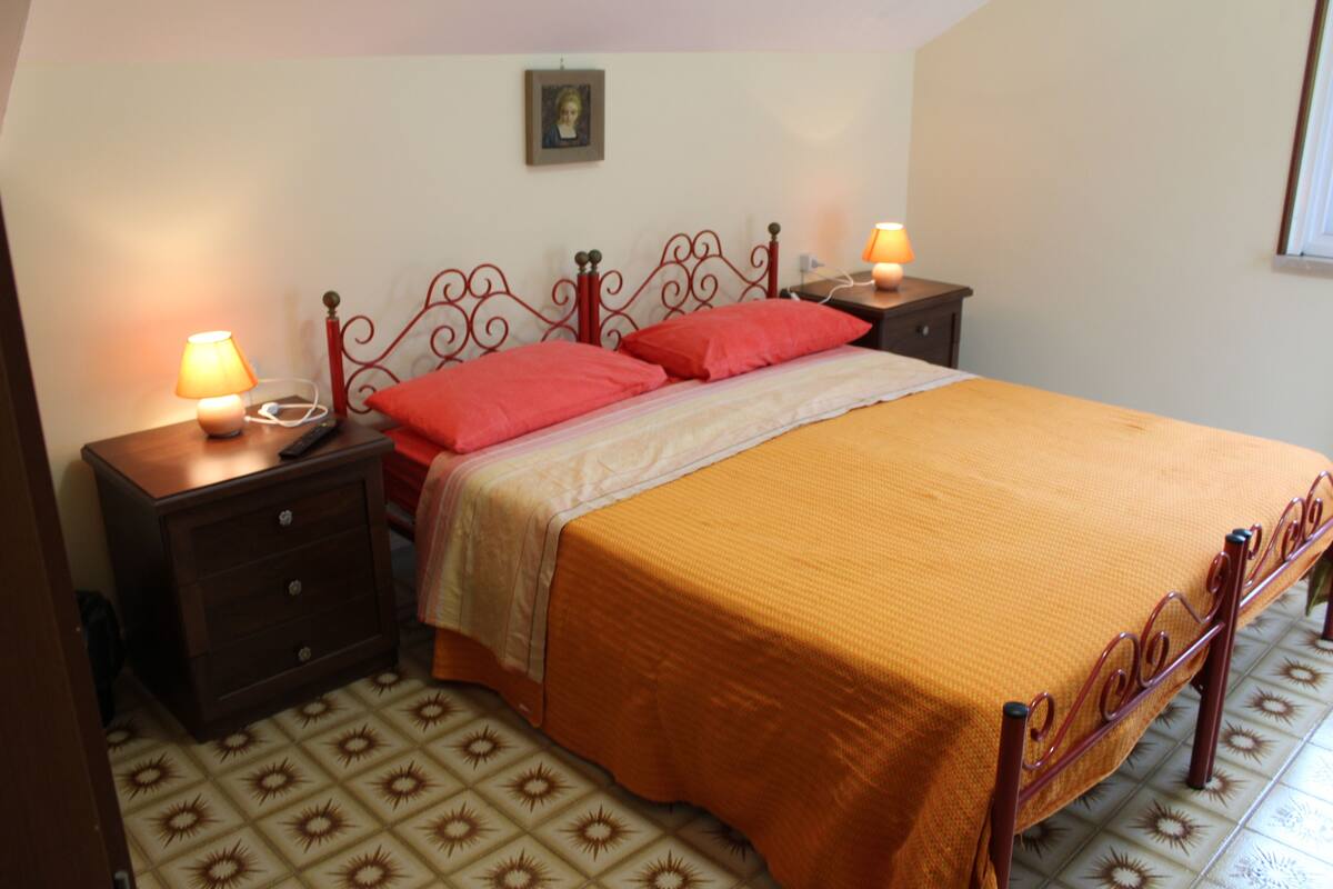Un dormitorio con una cama, dos mesitas de noche, una lámpara y un suelo estampado.
