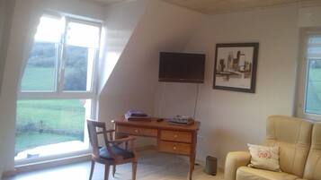 Ein Zimmer mit Schreibtisch, Stuhl, Fernseher und einer Couch.