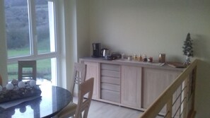 A kitchen with a dining table, chairs, and a view of the outdoors through large windows. - Aux vignes (Wissembourg)
