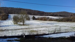 A snow-covered landscape with a river, trees, and a hilly background. - Aux vignes (Wissembourg)
