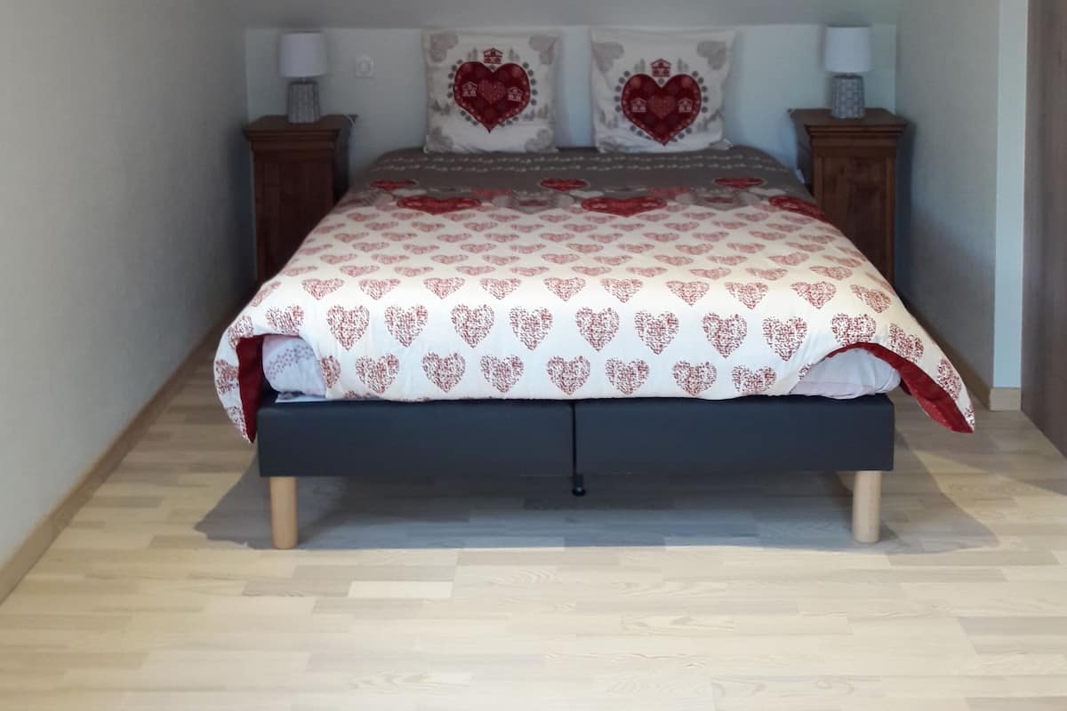 A bedroom with a wooden ceiling, a bed with a patterned bedspread, two bedside tables with lamps, and a framed picture on the wall.