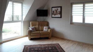 Una sala de estar con un sofá color beige, un tapete estampado, un televisor de pantalla plana y ventanas amplias.