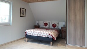 Un dormitorio con techo inclinado, una cama con ropa de cama estampada con corazones, una mesita de noche, una lámpara y un cuadro enmarcado en la pared.