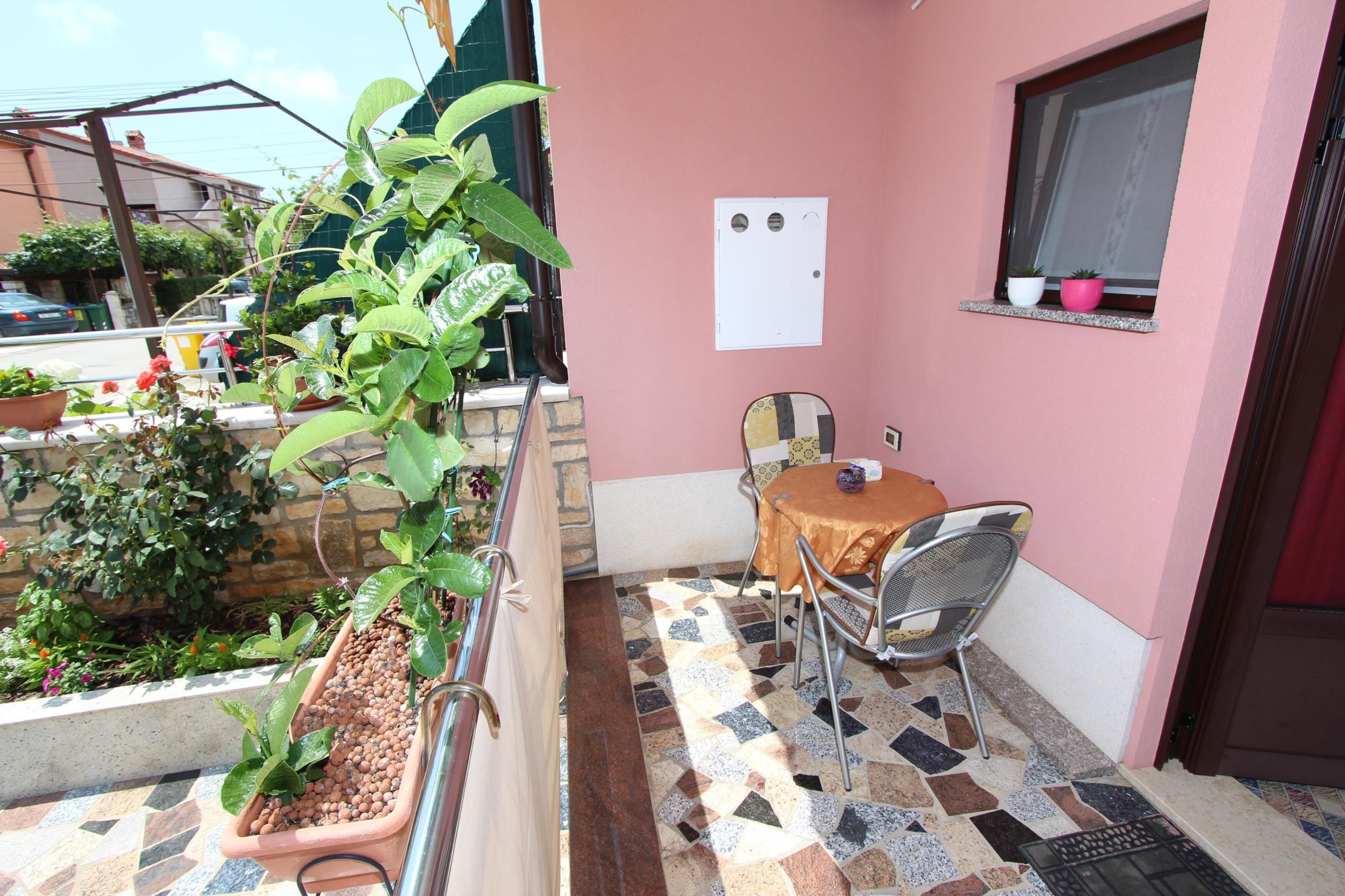 A balcony with a table and chairs, potted plants, and a tiled floor.