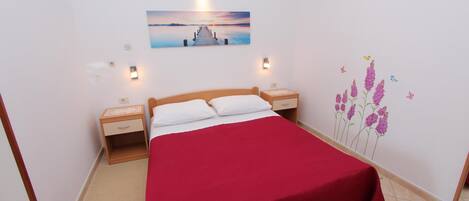 Ein Schlafzimmer mit einem hölzernen Bett, einer roten Bettdecke, zwei Nachttischen, einem Wandbild und einer Blumen-Wandsticker.