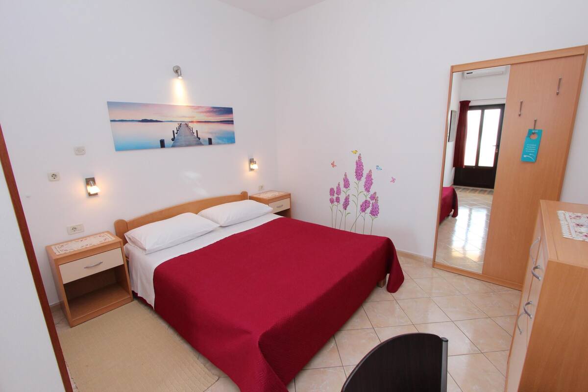 Un dormitorio con cama, mesita de noche, cómoda, espejo y un cuadro colgado en la pared.