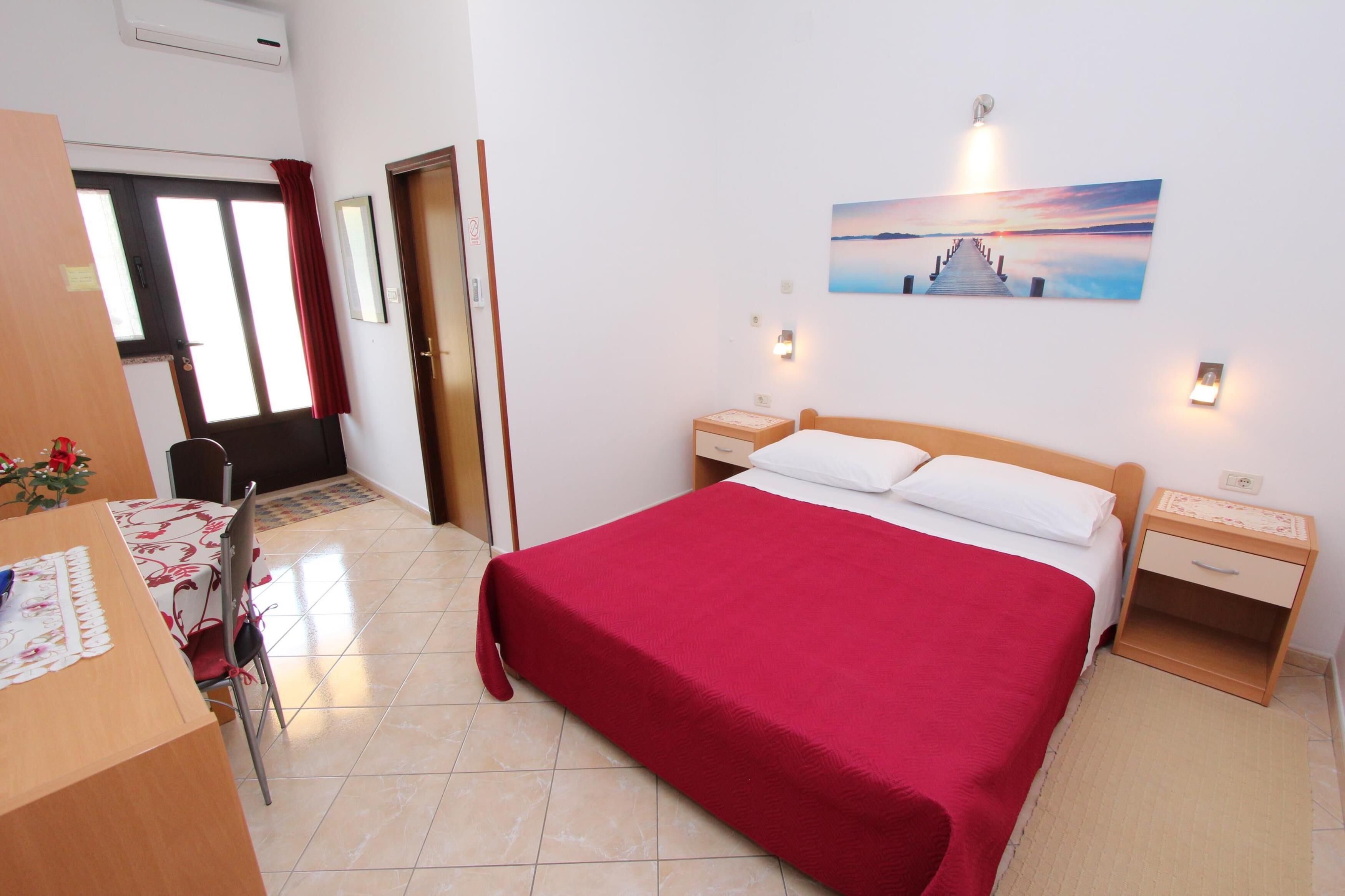 A hotel room with a large bed, a desk with a chair, a nightstand, and a wall-mounted picture.