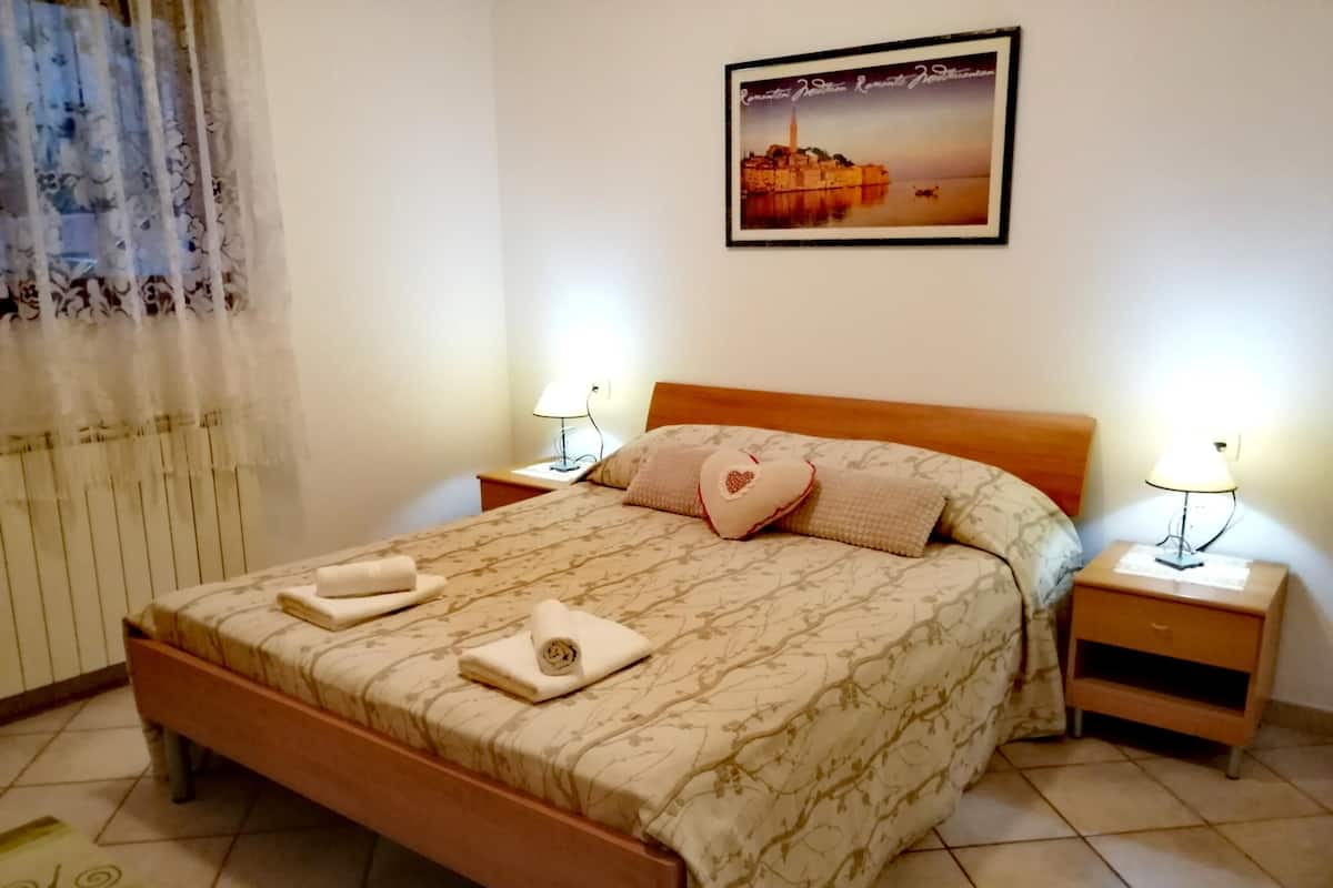 Una cama bien hecha con un edredón estampado, dos lámparas de noche y un cuadro en la pared.