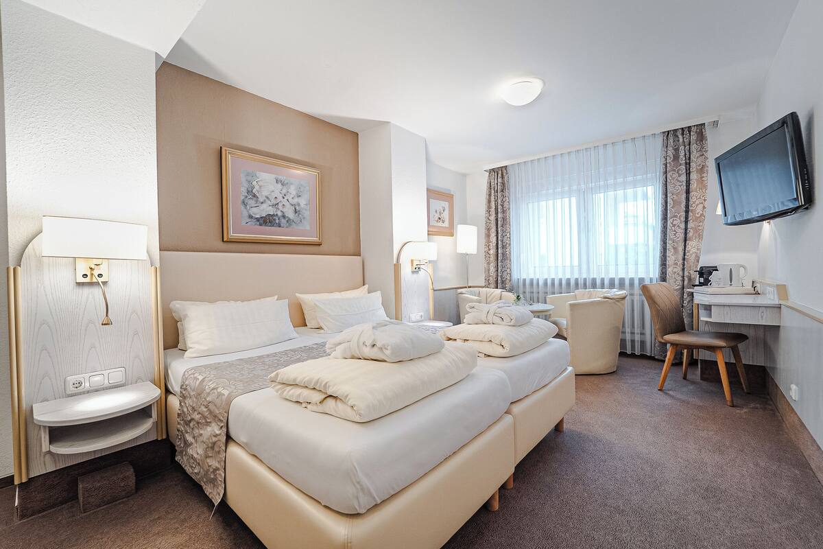 A hotel room with a large bed, a desk, a chair, a TV, and a window with curtains.