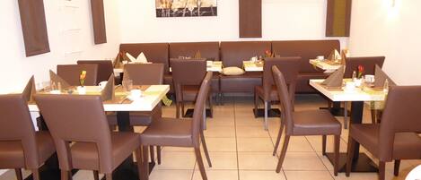 A restaurant with booths and tables, each with a menu, cutlery, and a vase with flowers.