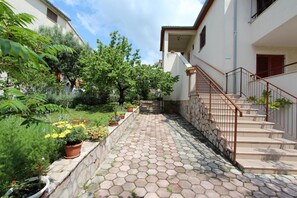 A paved pathway leading to a staircase with a railing, surrounded by potted plants and greenery.