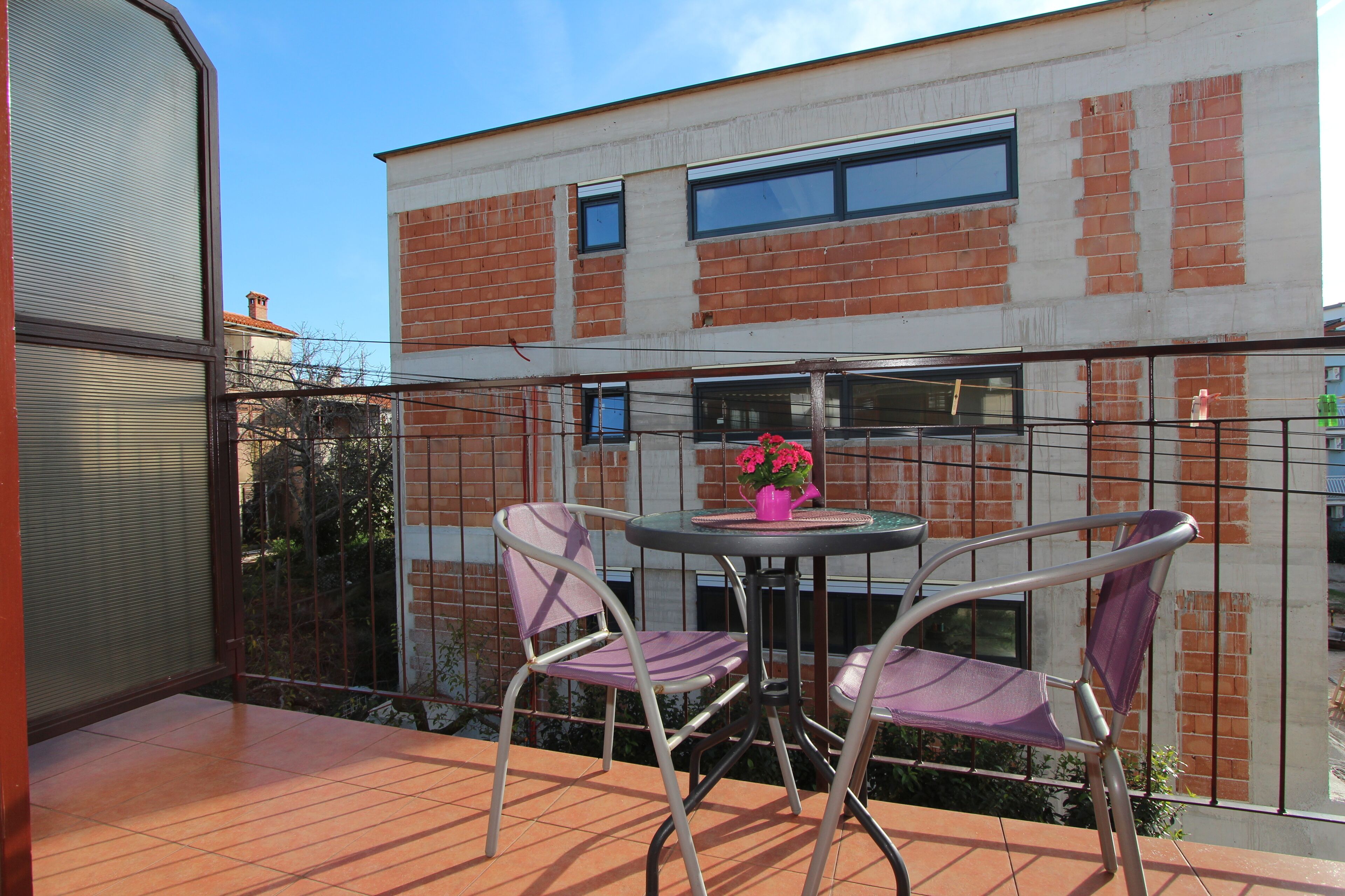 A balcony with a table and chairs, a potted plant, and a view of a brick building.