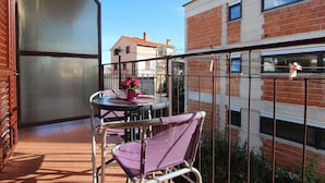 A balcony with a table and chairs, a potted plant, and a view of a brick building. - Guests House Sanja (Rovinj)