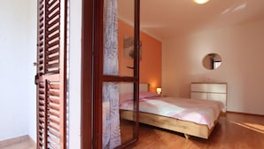 A bedroom with a wooden bed, a nightstand, a mirror, and a sliding glass door. - Guests House Sanja (Rovinj)