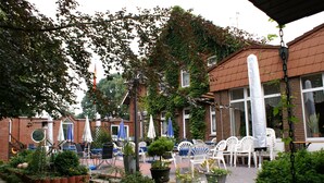 A patio area with outdoor seating, potted plants, and a brick building with windows. - Kluster Hof (Basdahl)