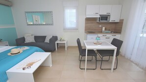 Una habitación de hotel compacta con cama, una pequeña mesa de comedor, kitchenette y un rincón de descanso.