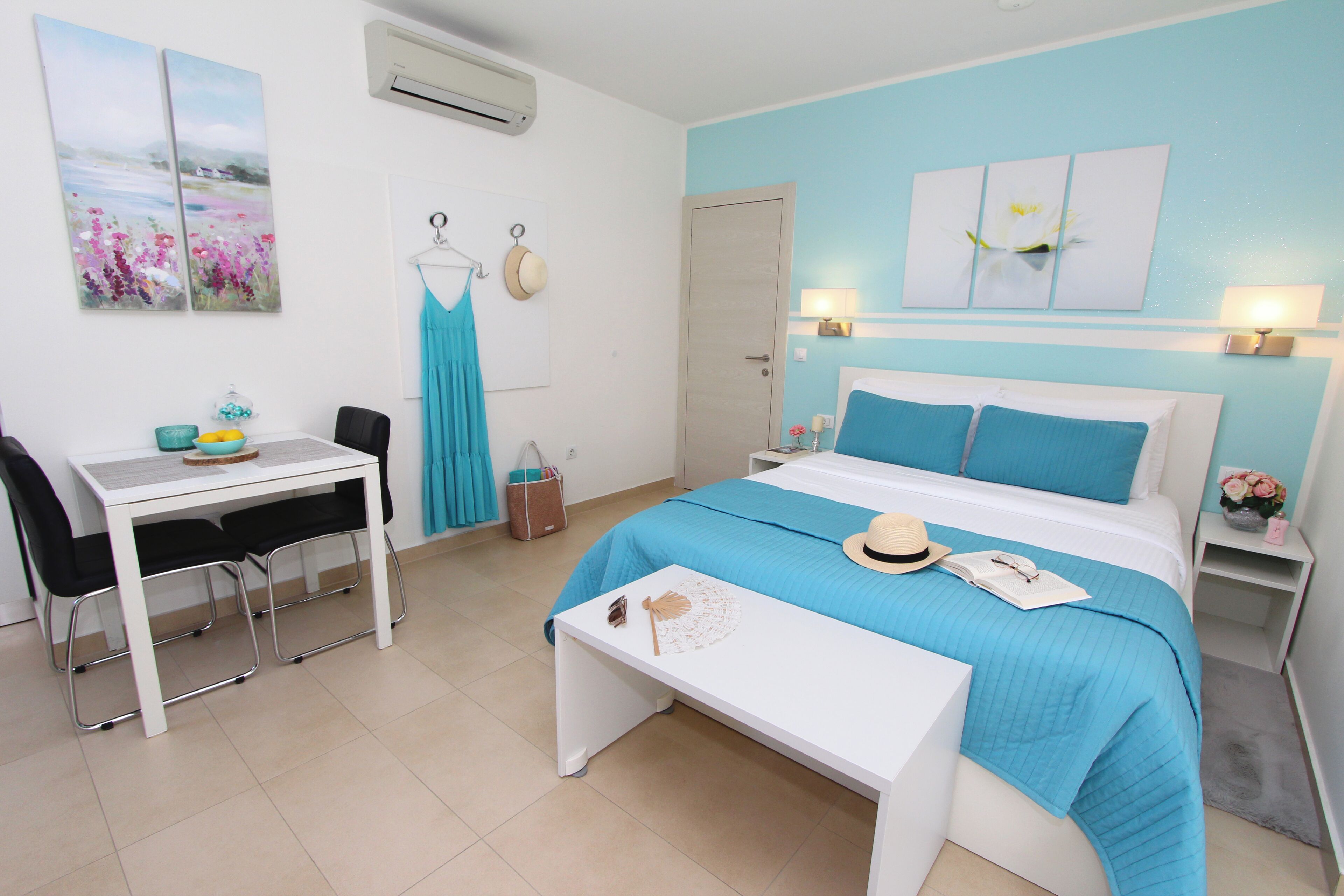 A bedroom with a bed, a desk, chairs, a table, and artwork on the walls.