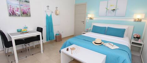 A bedroom with a bed, a desk, chairs, a table, and artwork on the walls.