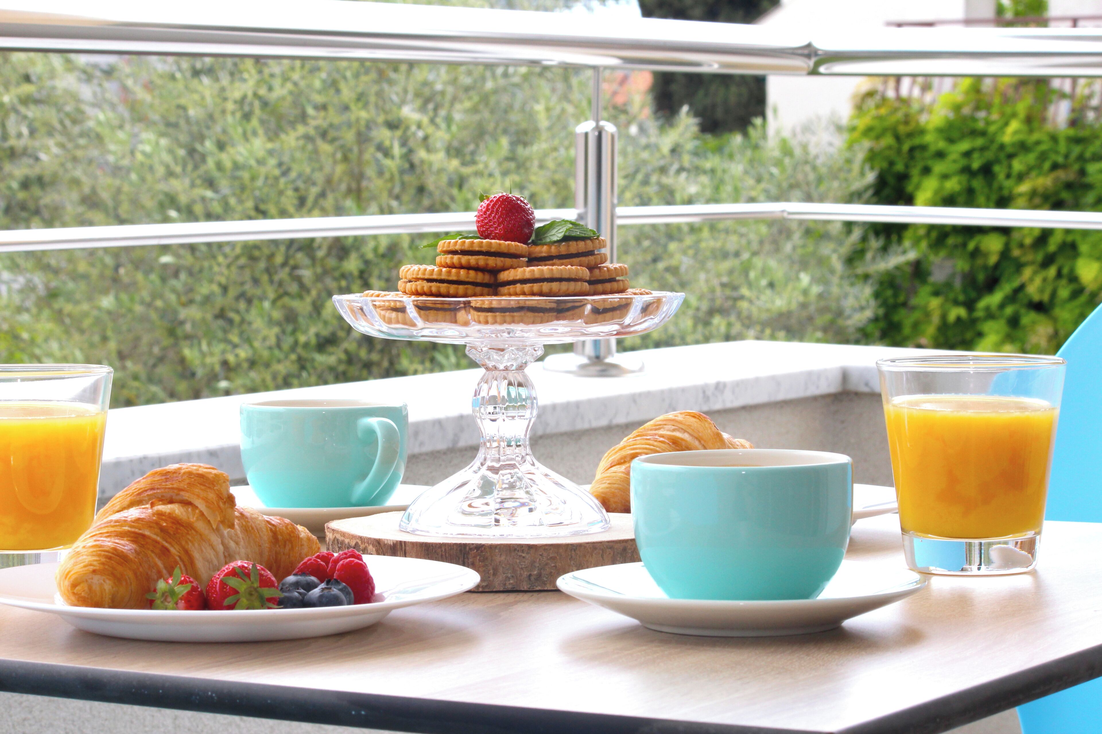 A breakfast setting with croissants, berries, and juice glasses on a balcony with a view.